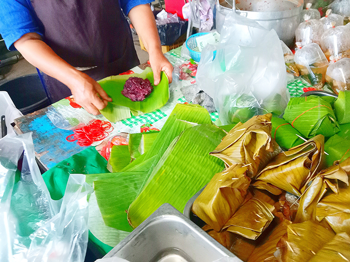 バナナの葉に熱々のもち米を入れて手作業で包んでいる様子